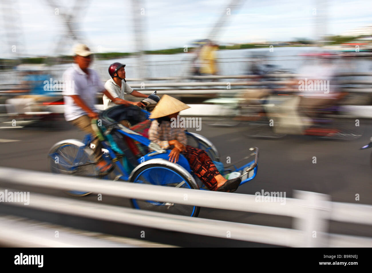 Scena di strada. moto, panning, blur. Donna con il tradizionale cappello conico avente un giro in cyclo. Tinta, Vietnam. SE L'Asia Foto Stock