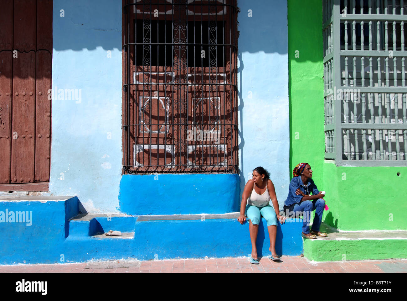 Due donne sedute sulla scaletta nella parte anteriore del case qith gated windows Camaguey Cuba Foto Stock