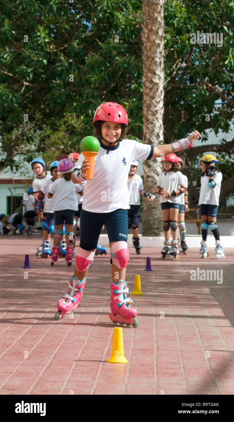 Team di junior school girl alunni competere in slalom rollerblade corso con la palla e la tazza di concorrenza di bilanciamento Foto Stock