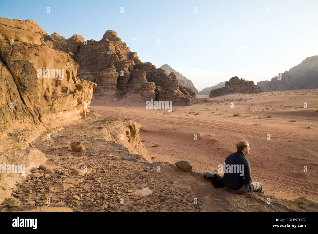 Un turista si siede a guardare il tramonto nel deserto, Wadi Rum, Giordania Foto Stock