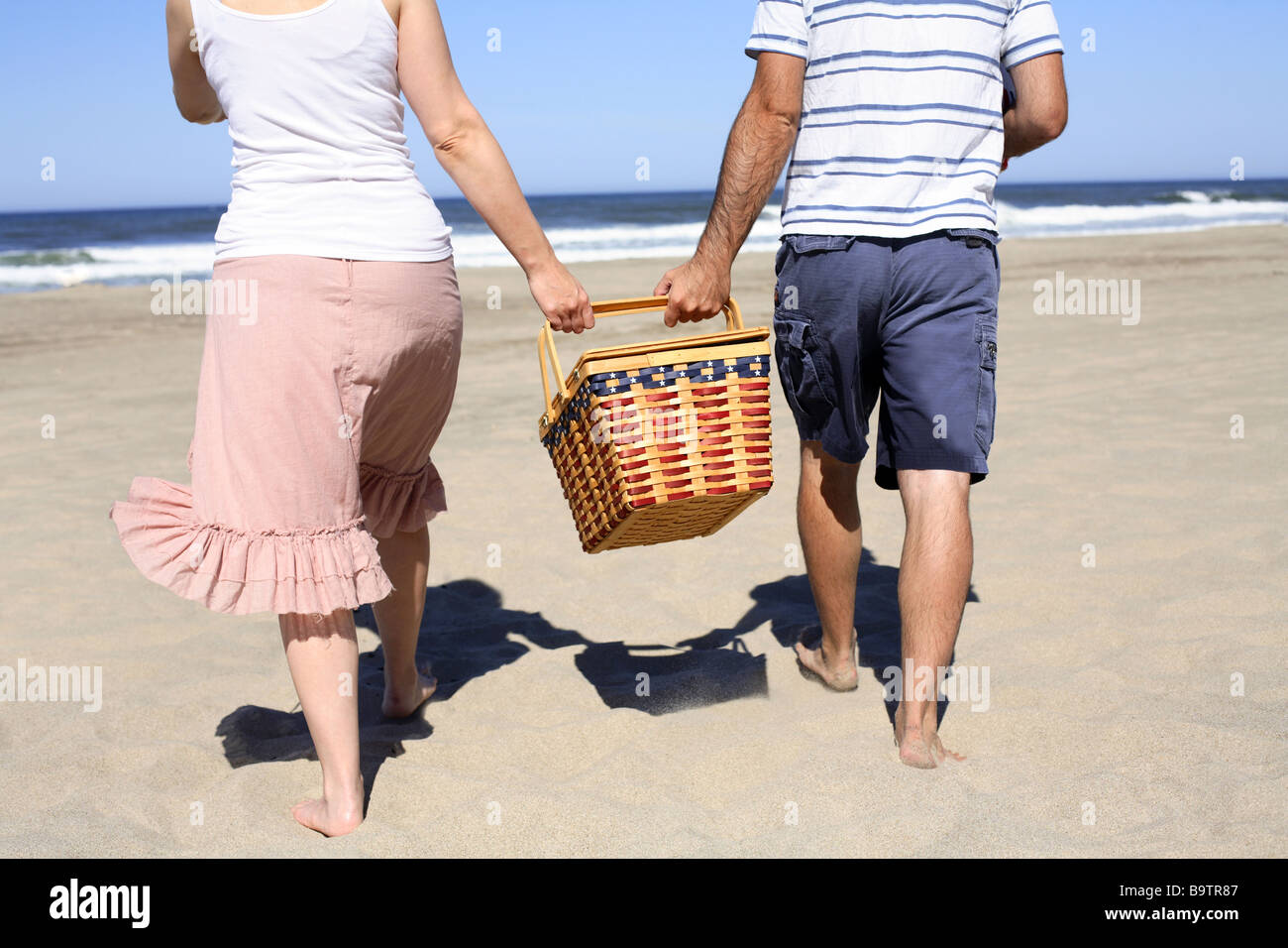 Giovane camminando sulla spiaggia con cesto per pic-nic Foto Stock