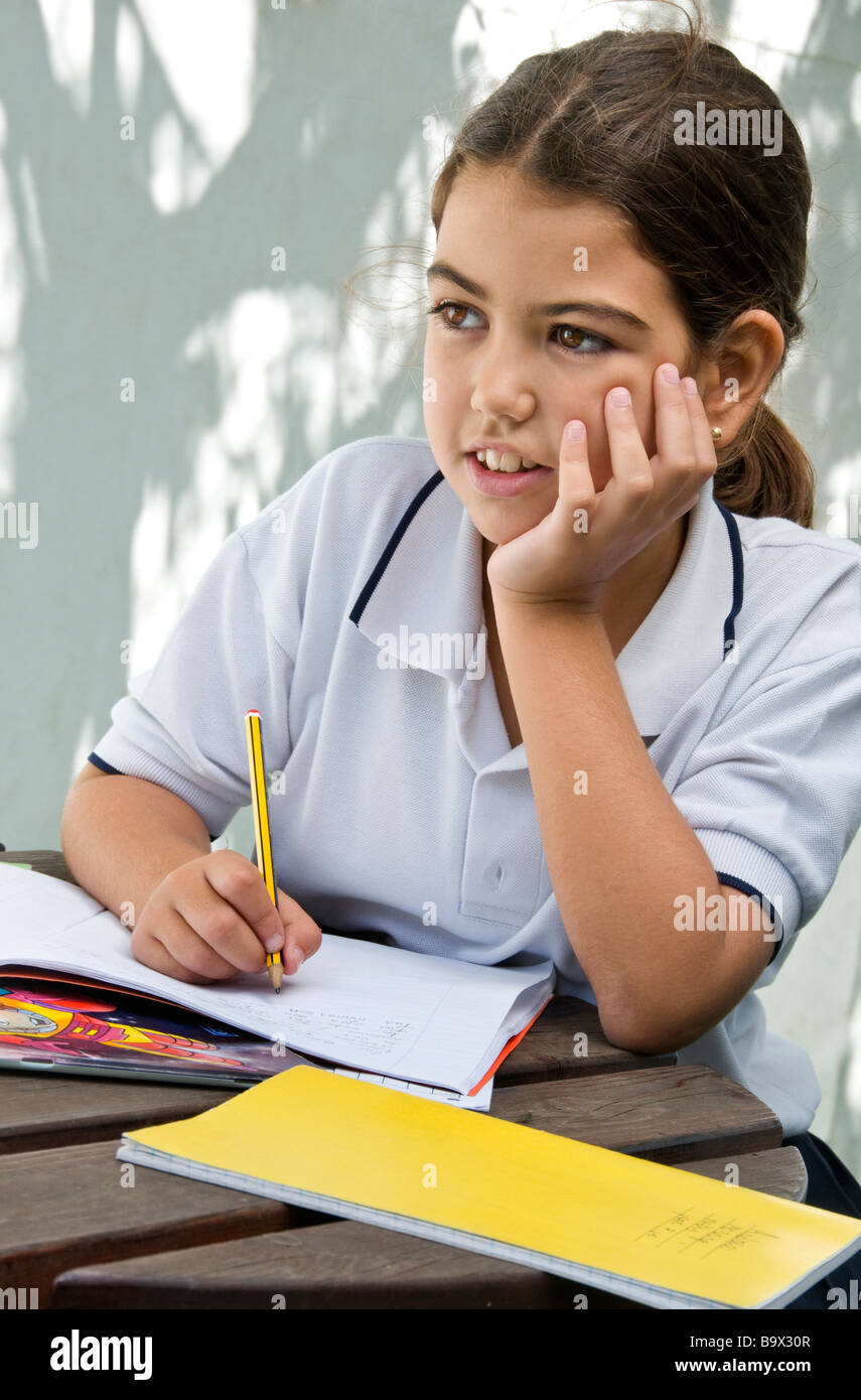 Junior medio schoolgirl pause nel pensiero durante i suoi studi informale al di fuori sul soleggiato Campo giochi scuola campus Foto Stock