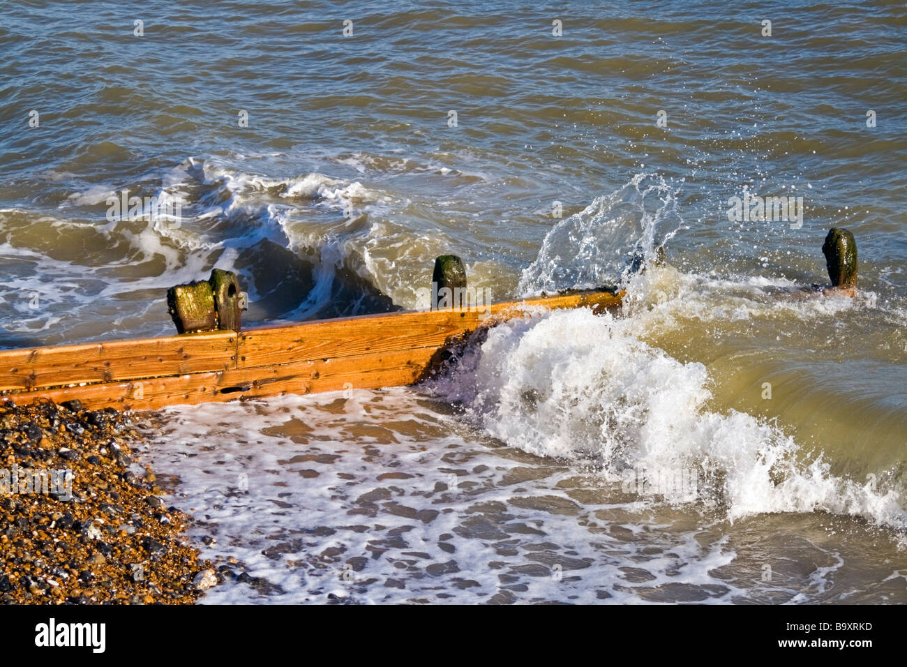 Ondata di schiantarsi su una struttura di frangionde su di una spiaggia di ciottoli. Foto Stock