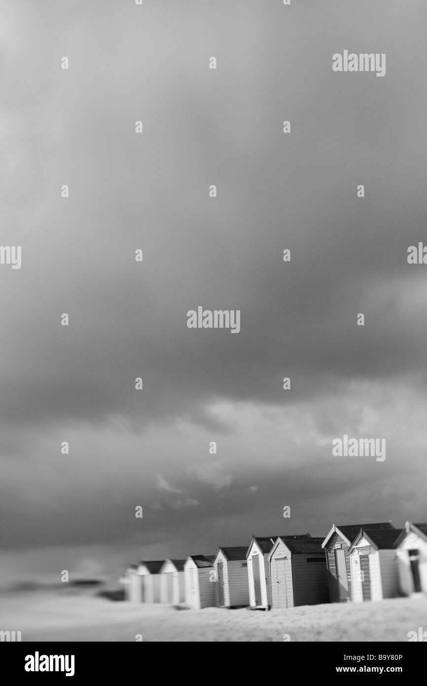 Cabine sulla spiaggia, sotto il sole, ma con le nuvole pesanti provenienti oltre. Immagine in bianco e nero con un big sky. Foto Stock