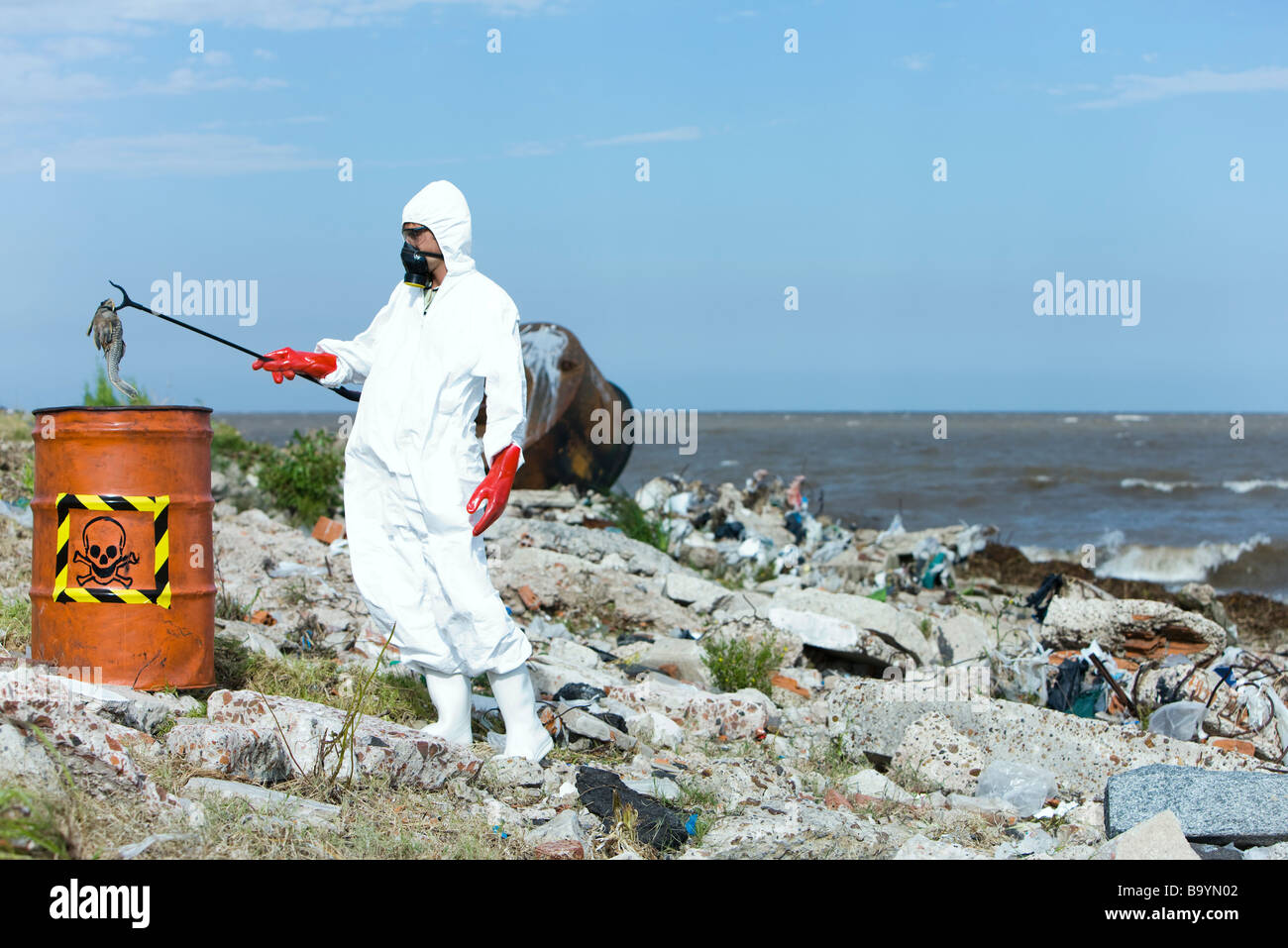 Persona in tuta protettiva mettendo i pesci morti in rifiuti pericolosi canna Foto Stock