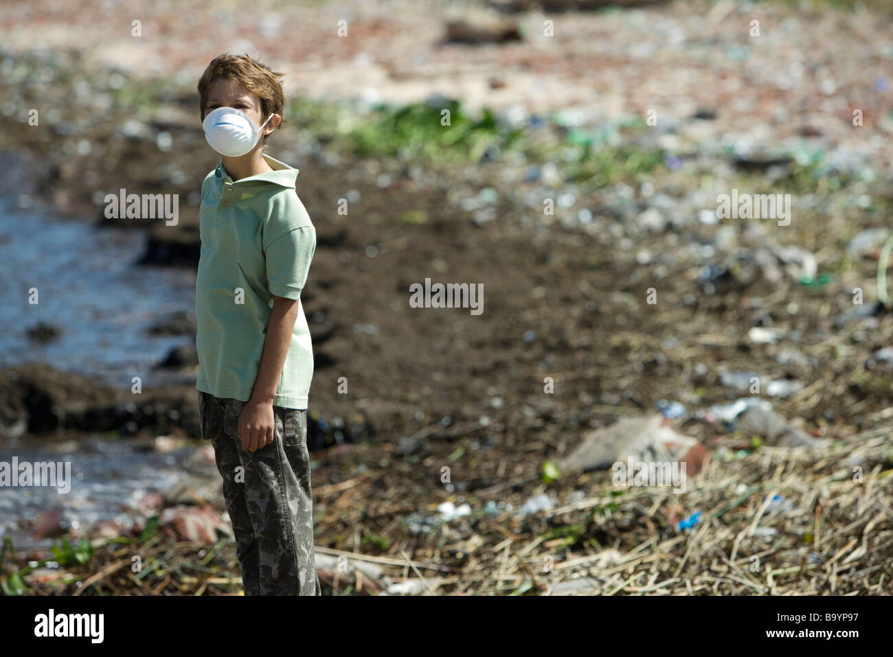Ragazzo in piedi sulla riva inquinati, indossa una maschera di inquinamento Foto Stock