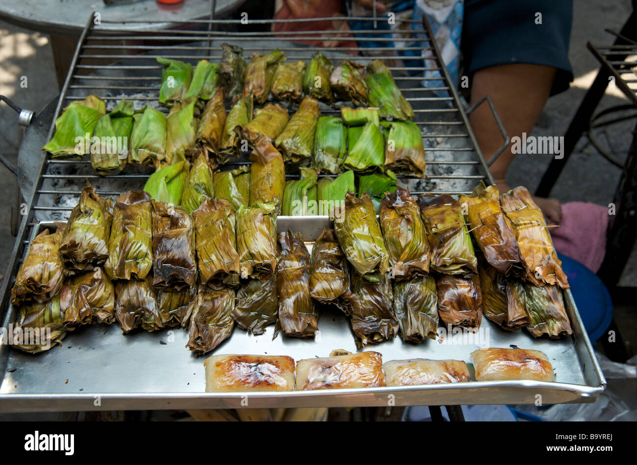 Primo piano di pacchi grigliati di banane avvolte nelle loro foglie su una bancarella di Bangkok Foto Stock