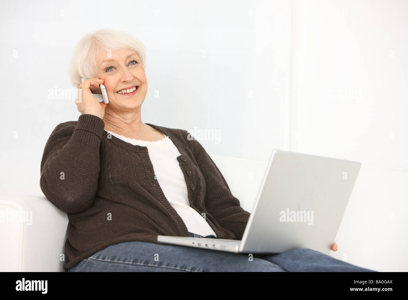 Senior donna con notebook parlando al cellulare Foto Stock