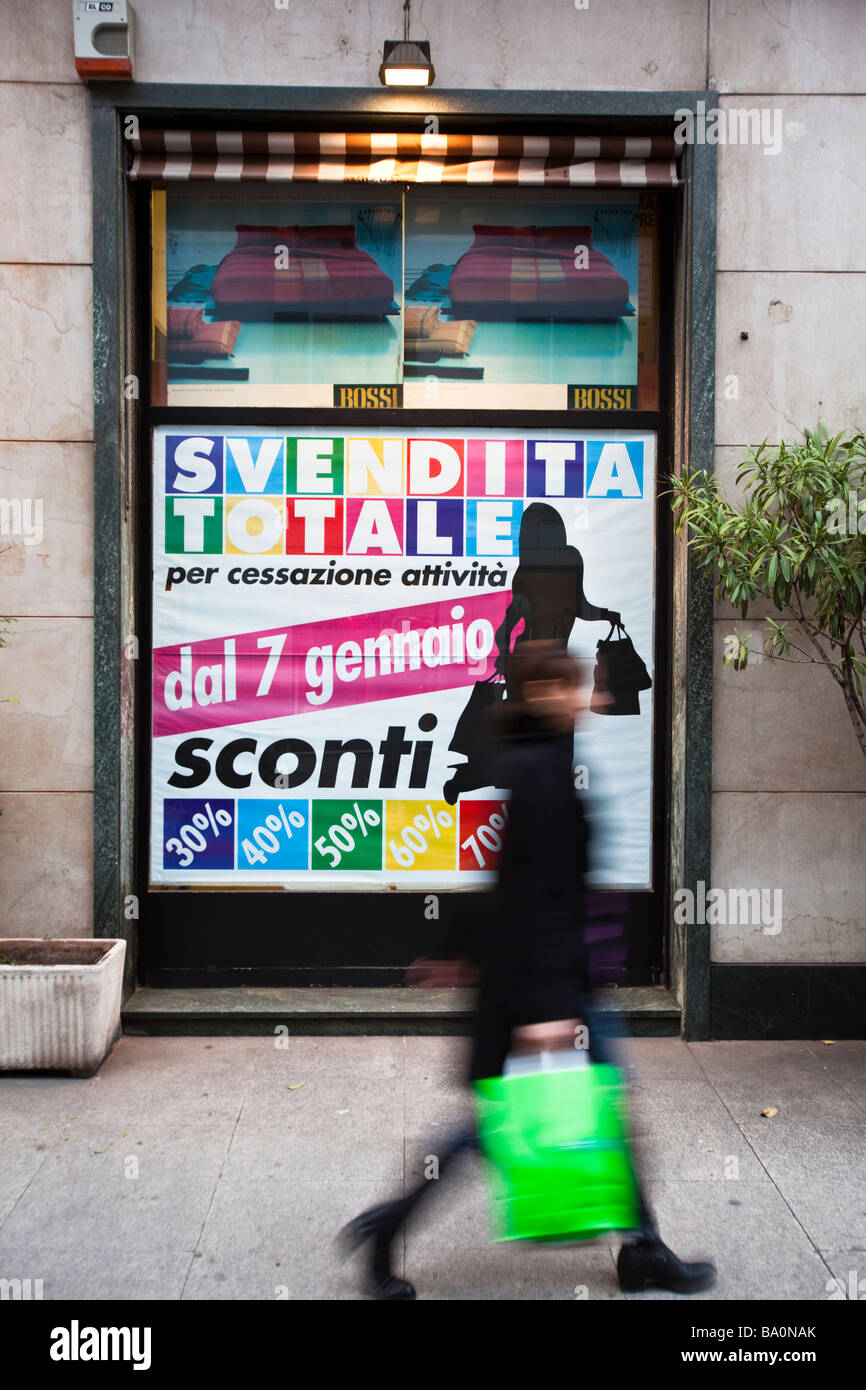 La donna passa da poster leggere 'Sales fino al 30%, 40%, 50%, 60%, 70% off' nella vetrina di un negozio di Como, Lombardia, Italia Foto Stock