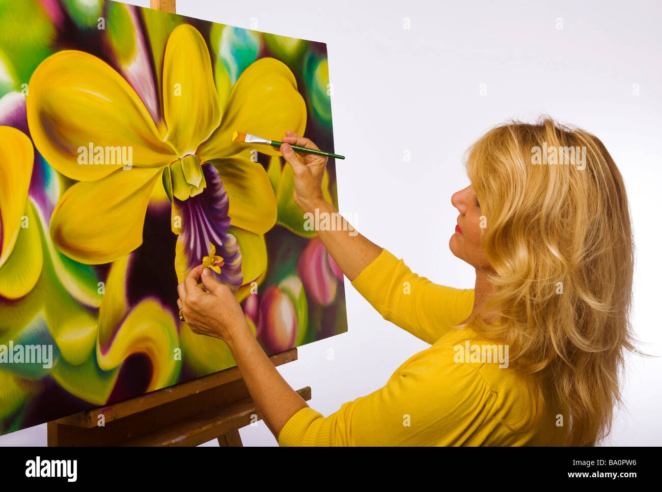Un artista femminile pittura dendrobium orchidee su tela nel suo studio Foto Stock