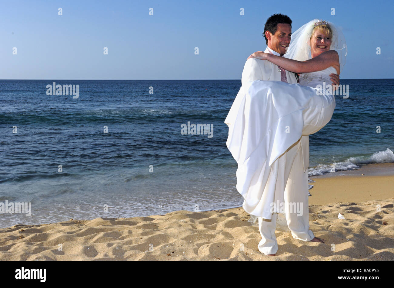 Lo sposo portando nuovo sposa sulla sabbiosa tropicale spiaggia dei Caraibi Grenada Foto Stock