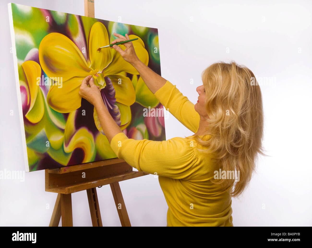 Un artista femminile pittura dendrobium orchidee su tela nel suo studio Foto Stock
