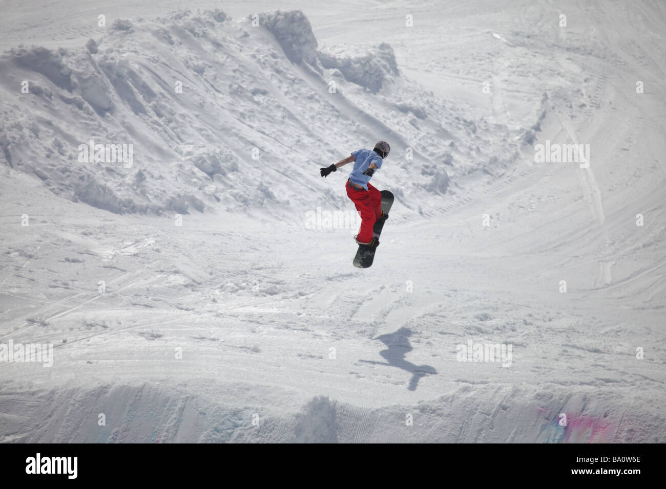 Un snow boarder jumping con la sua ombra che mostra l'altezza del salto in una giornata di sole Foto Stock