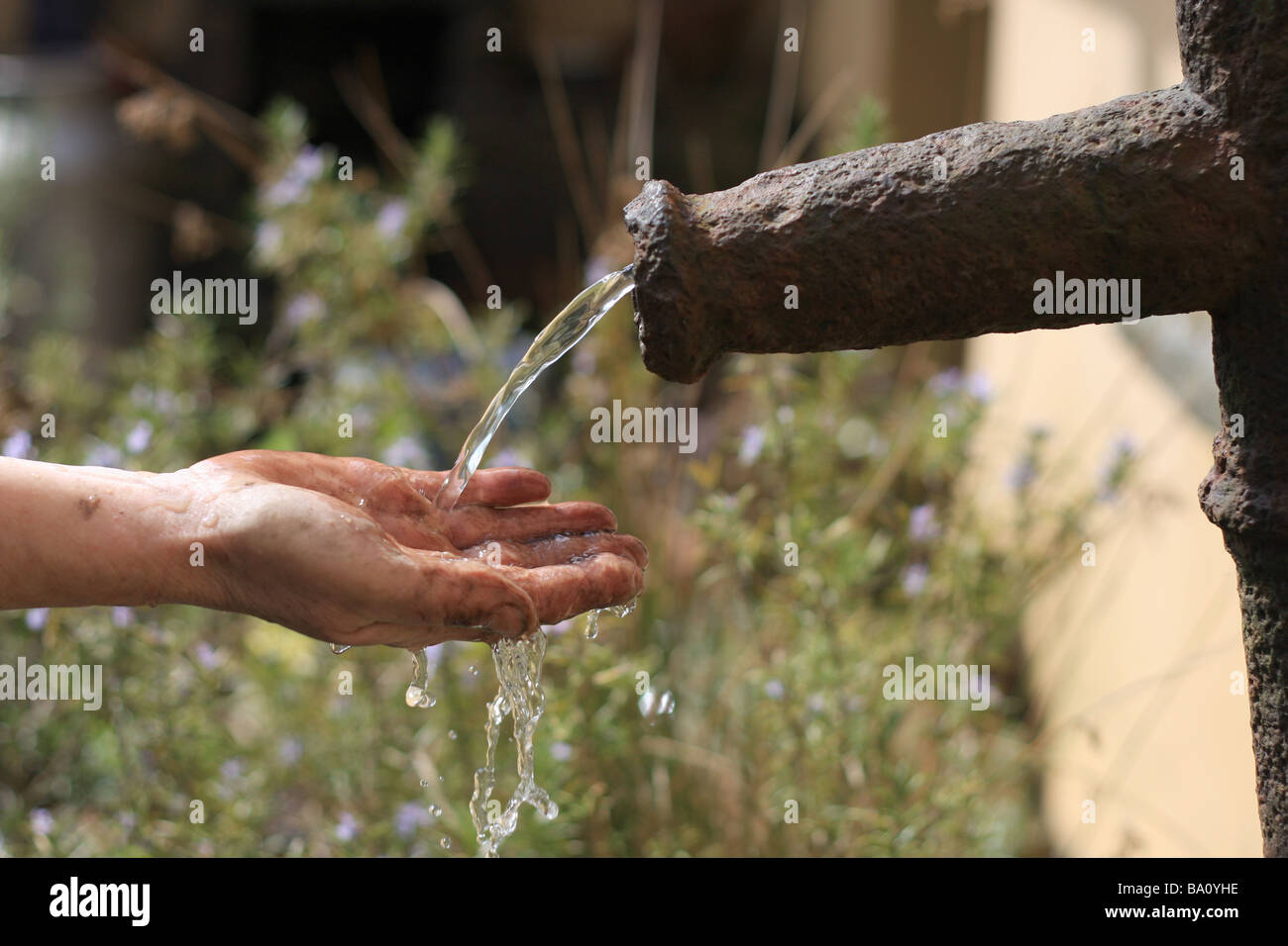 La donna lava la sporcizia fuori la sua mano utilizzando acqua da una vecchia pompa di ferro. Foto Stock