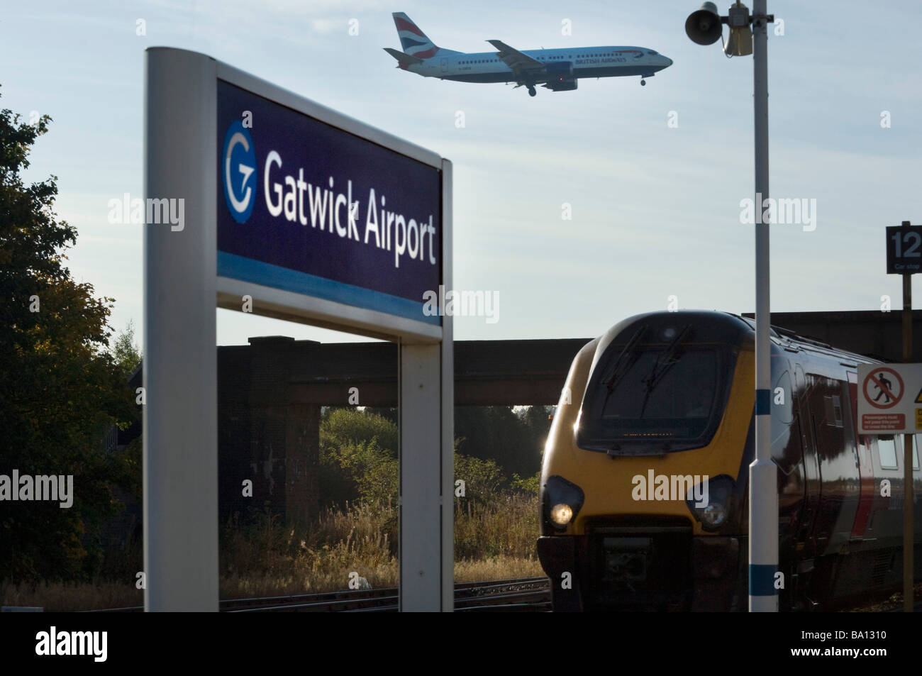 Un British Airways piano terre sopra la stazione ferroviaria dell'aeroporto di Gatwick in treno arriva al di sotto di esso. Foto Stock