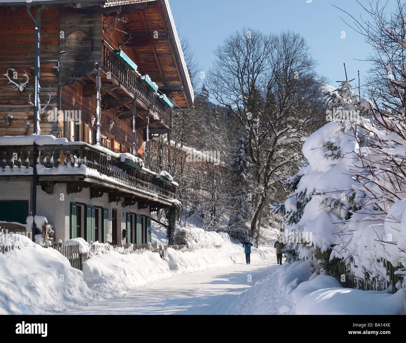 In legno tipico casa austriaca in inverno giornata soleggiata con abbondanza di neve e il cielo blu e due walker figlio la strada Foto Stock