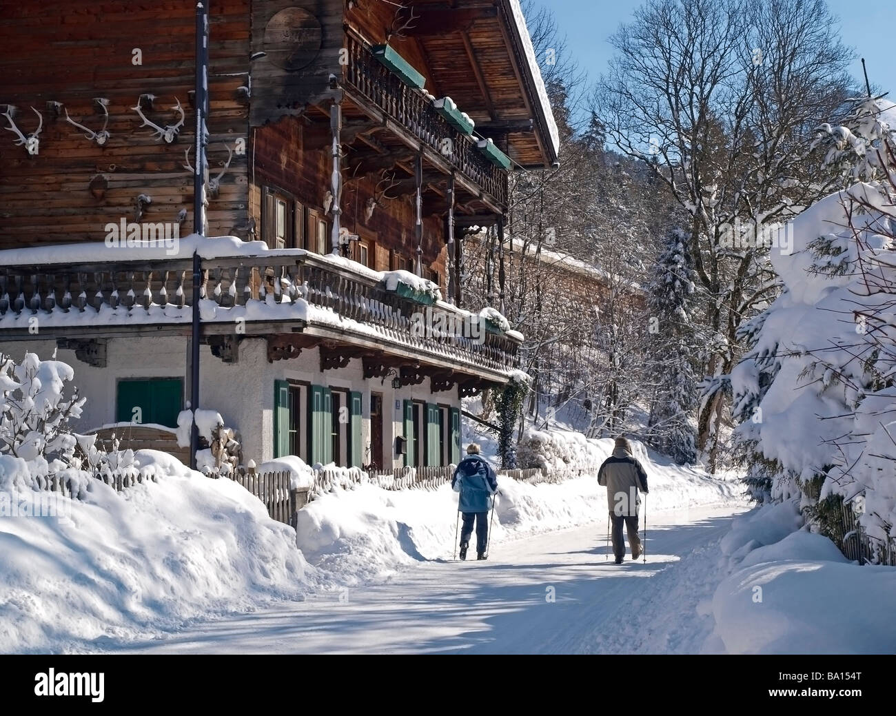 In legno tipico casa austriaca in inverno giornata soleggiata con abbondanza di neve e il cielo blu e due walker figlio la strada Foto Stock
