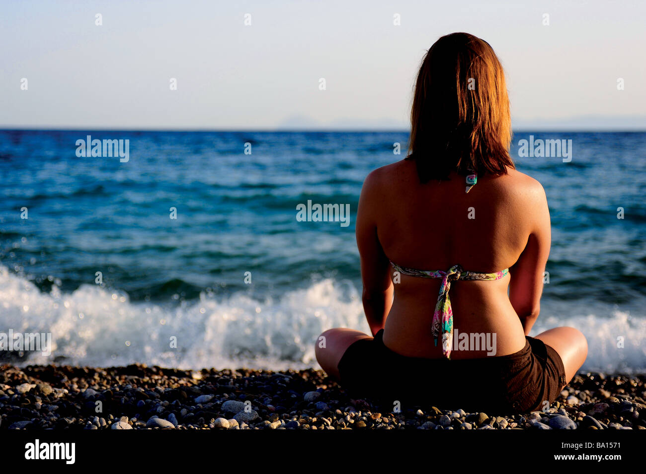 Una giovane donna seduta su una spiaggia che si affaccia sul mare Foto Stock