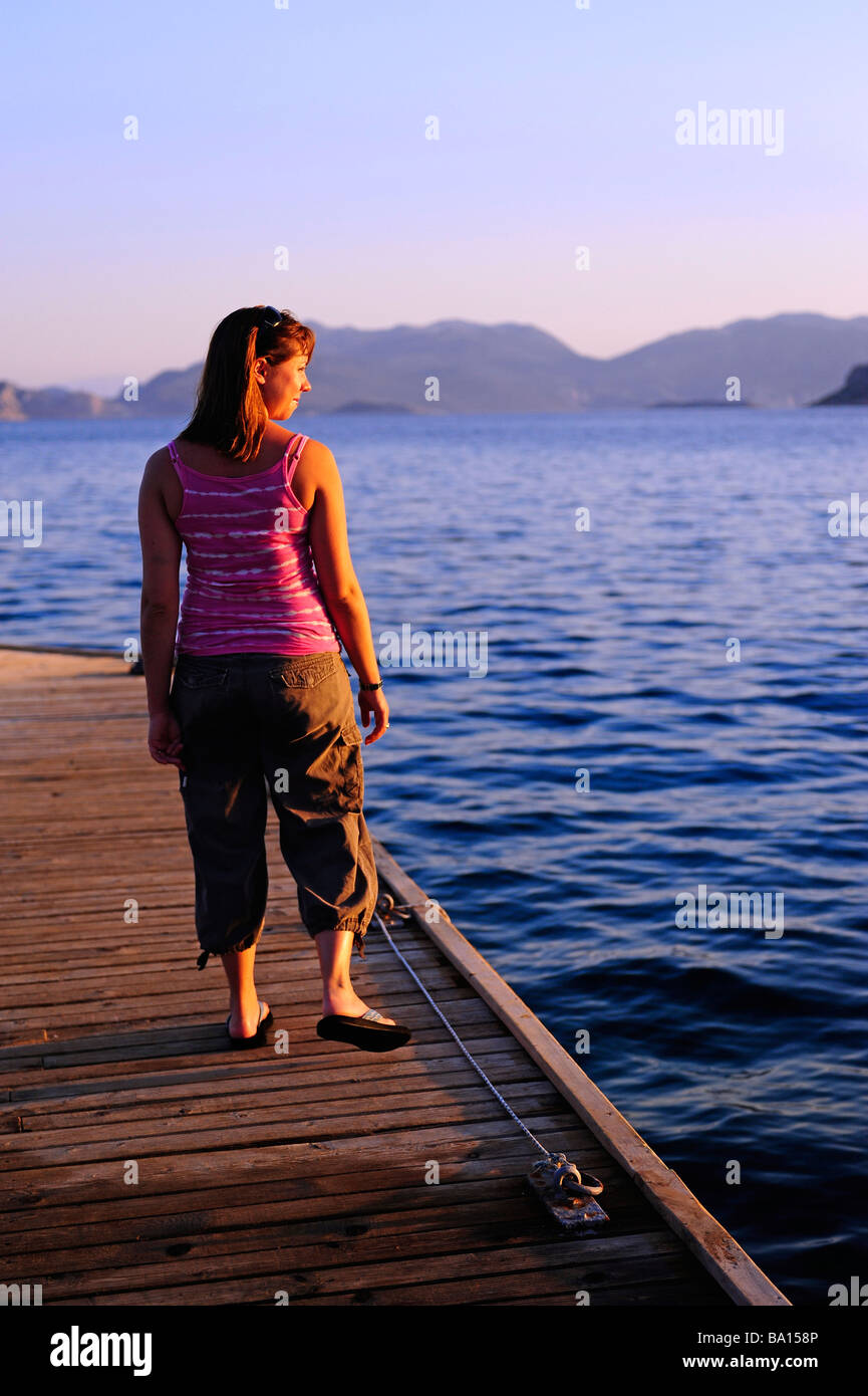 Una giovane donna in piedi su un pontile che guarda sul mare Foto Stock