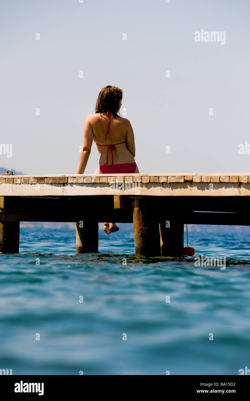 Una giovane donna seduta su un pontile che guarda sul mare Foto Stock