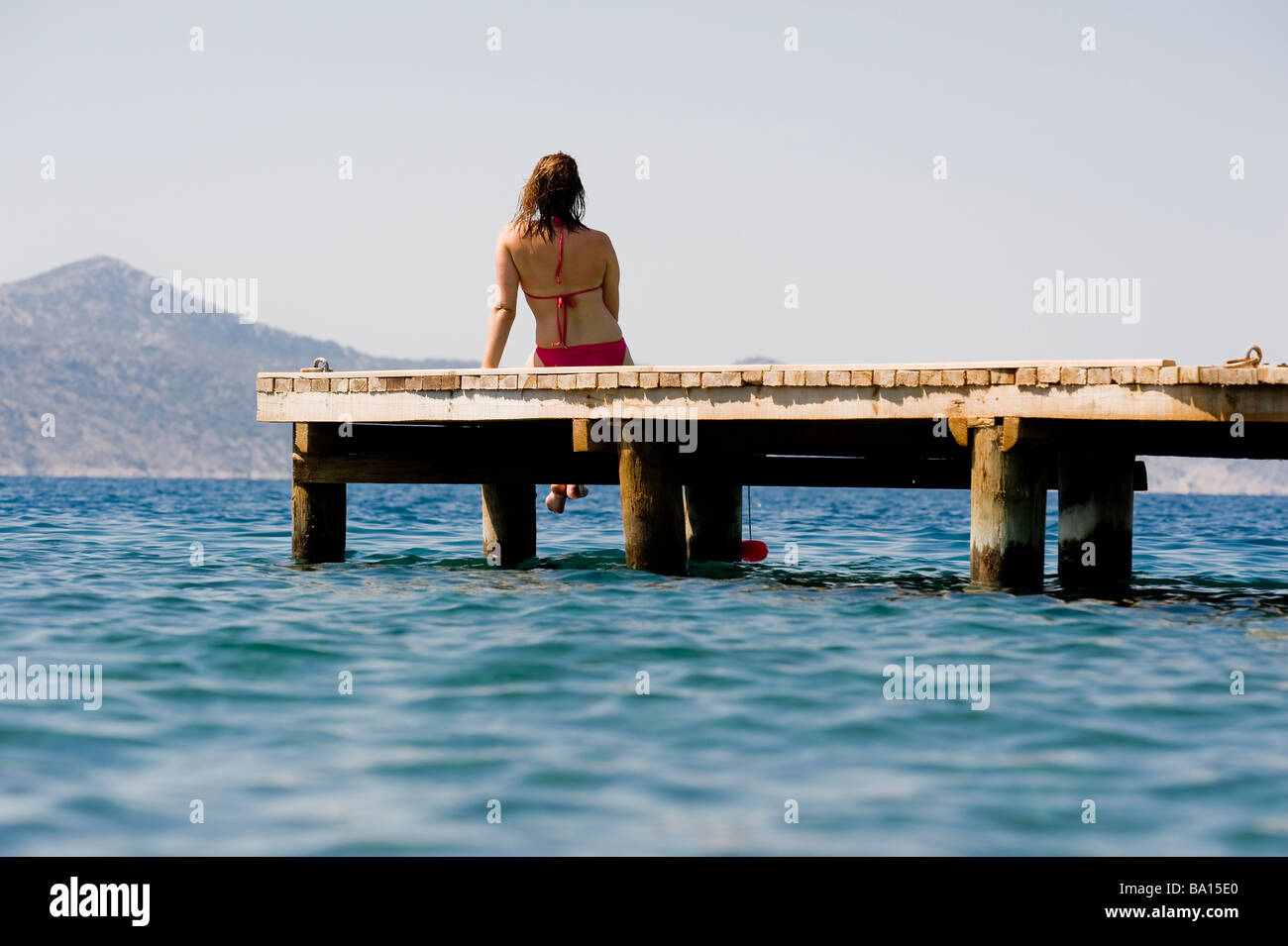 Una giovane donna seduta su un pontile che guarda sul mare Foto Stock