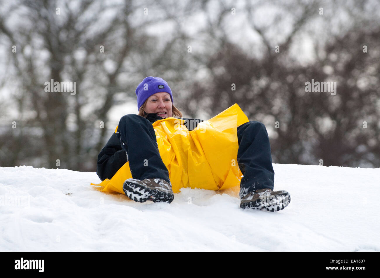 Donna di mezza età avendo divertimento slittino con un sacchetto bivvy Foto Stock