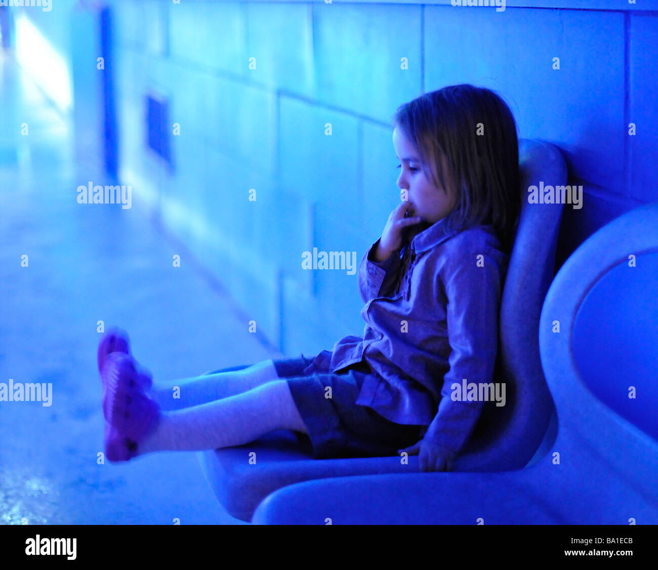 Bambino seduto e succhiare dita in illuminazione blu MR Foto Stock