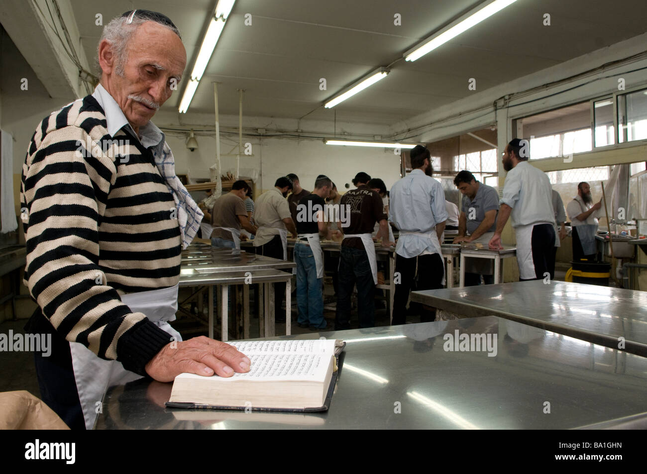 Un ebreo religioso prega mentre altri ebrei preparano Matzot tradizionale Pane azzimo mangiato durante la Pasqua al panificio Kfar Chabad Israele centrale Foto Stock