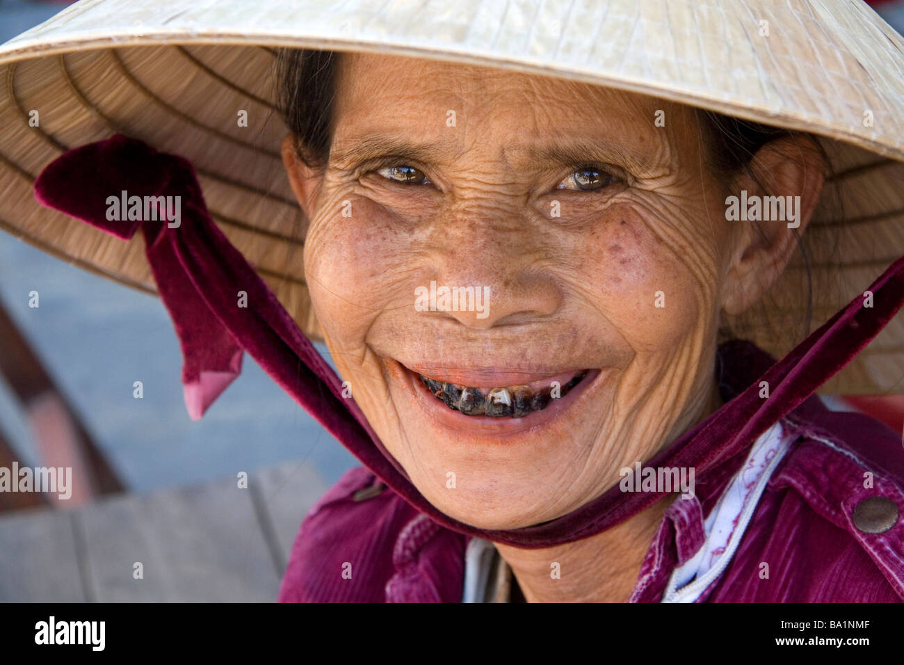 Ritratto di un'anziana donna vietnamita i cui denti sono macchiati da dado beetle indossando un cappello tradizionale in Hoi An Vietnam Foto Stock
