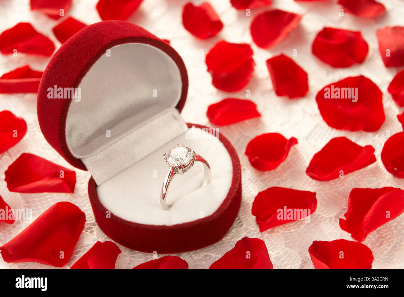 Anello di diamanti nel cuore scatola sagomata circondato da petali di rosa Foto Stock