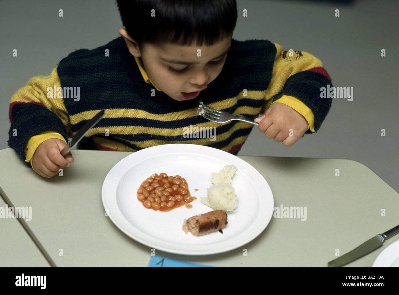 La scuola materna di boy eating bangers e ridurre in purea di fagioli Foto Stock