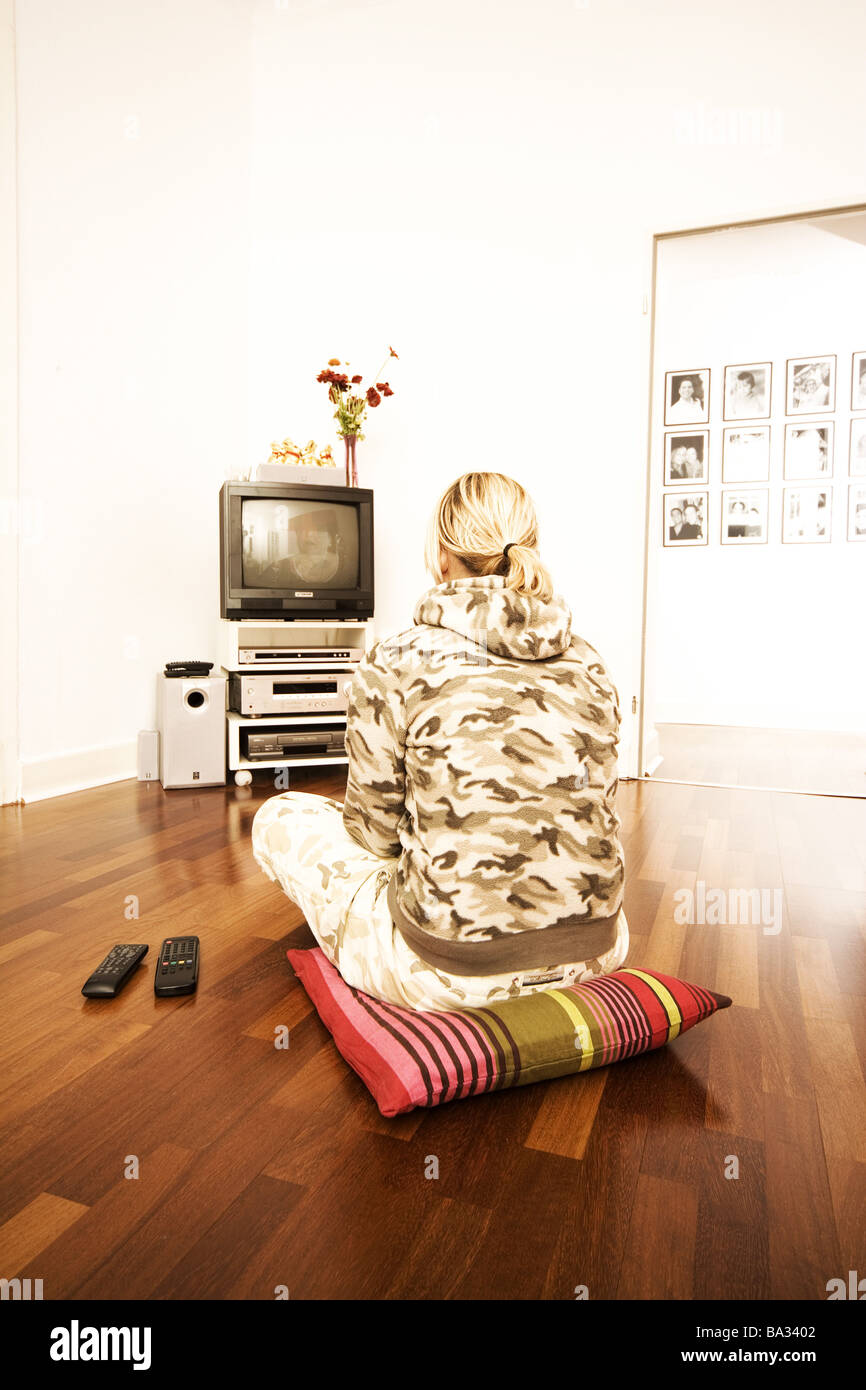 Si siede una donna giovane pavimento cuscini back-parere televisione-mostra persone 20-30 anni bionda camouflage-camicia con pavimento in legno, cuscini Foto Stock