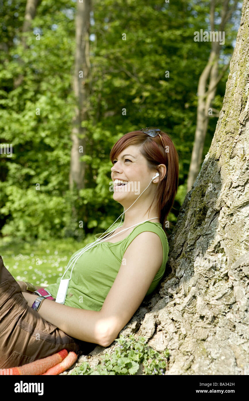 Donna giovane cuffie ascolta musica ride siede log si appoggia al lato persone serie 20-30 anni bella bruna attraente Foto Stock