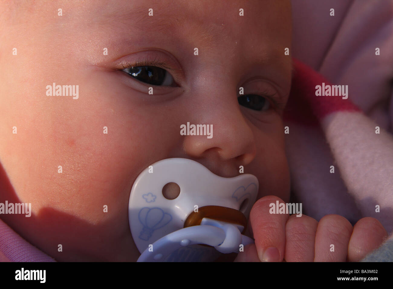 Un bambino con un manichino bianco nella sua bocca. Il lato del suo viso illuminato con luce del sole Foto Stock