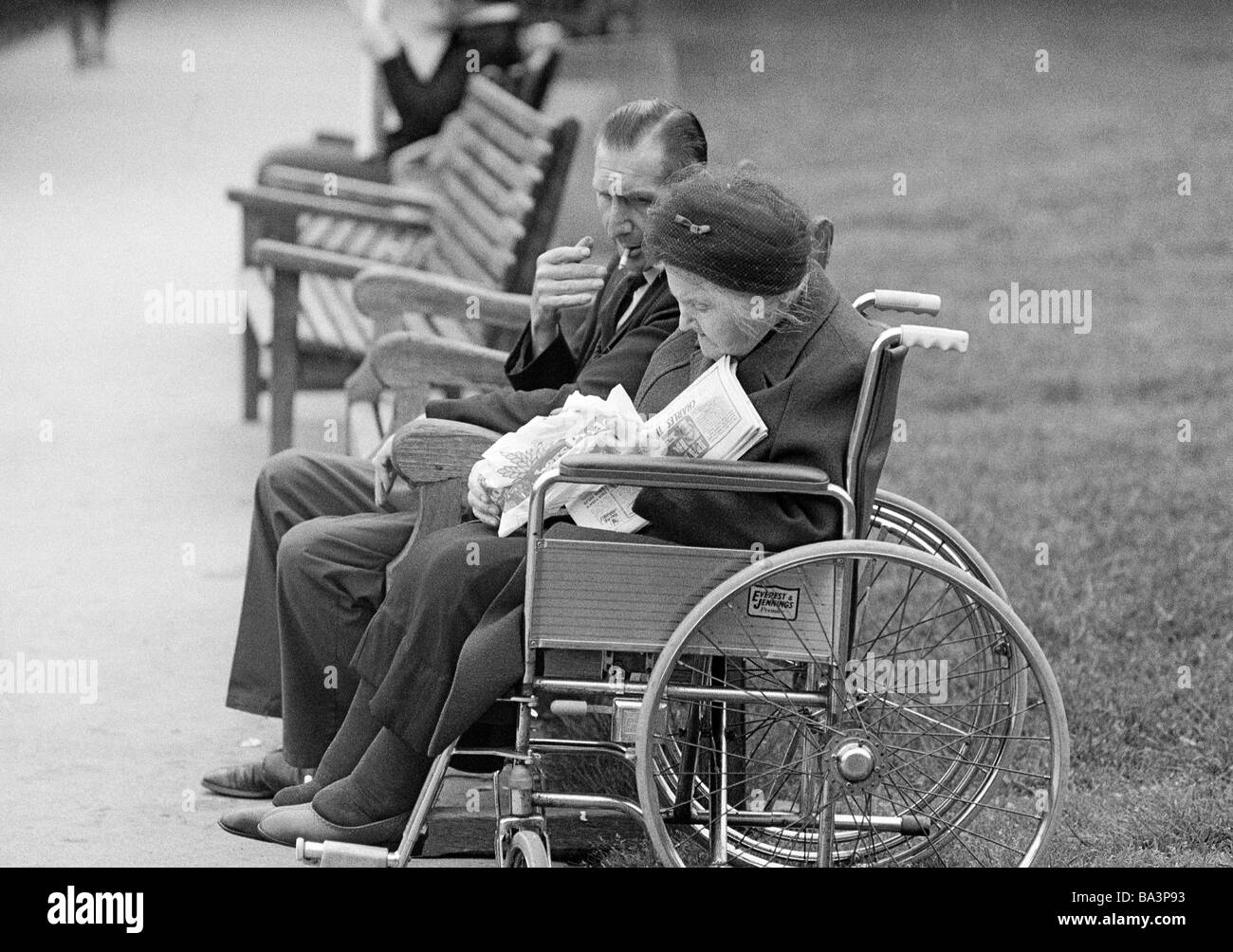 Negli anni settanta, foto in bianco e nero, persone di handicap fisici, la donna più anziana si siede nella sedia a rotelle, suo marito si siede accanto a lei su un banco, di età compresa tra i 65 e gli 75 anni, Gran Bretagna, Inghilterra, Londra Foto Stock
