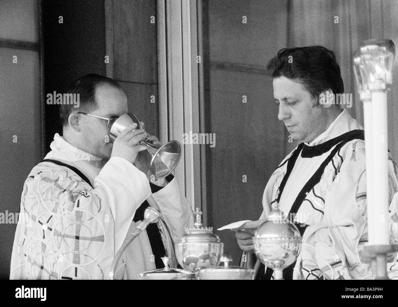Negli anni settanta, foto in bianco e nero, la religione, il cristianesimo, Santa Messa, eucaristia, accolito beve vino al di fuori della comunione cup, a parte il sacerdote, di età compresa tra 40 a 50 anni Foto Stock
