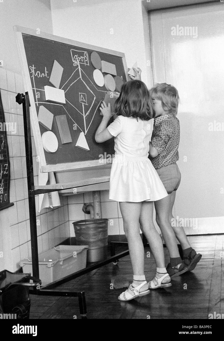 Negli anni settanta, foto in bianco e nero, di edificazione, scuola, scolari e studentesse in una scuola di classe durante le lezioni, i bambini di età compresa tra i 7 e i 10 anni, un ragazzo e una ragazza a una lavagna Foto Stock