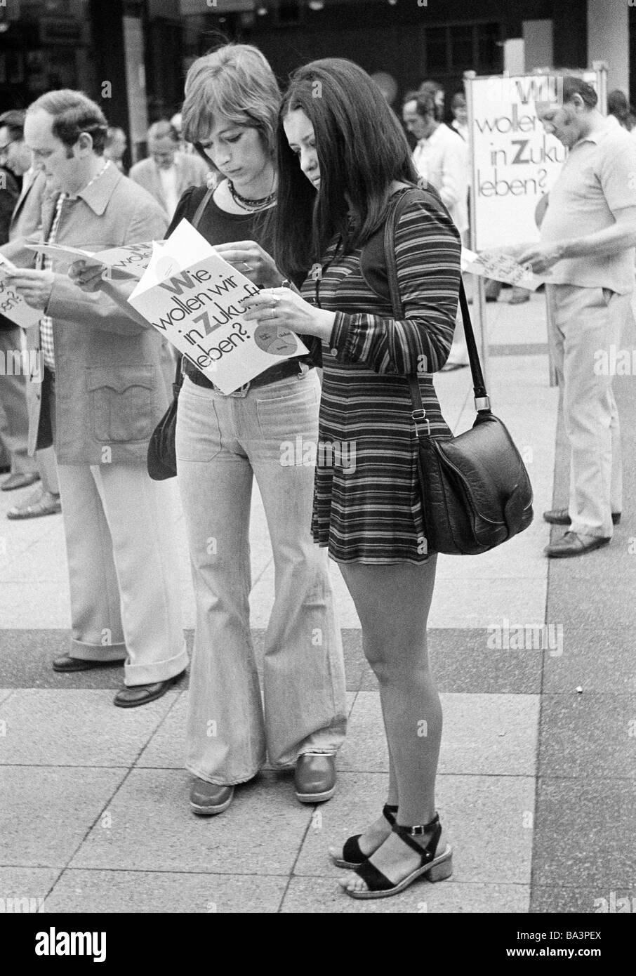 Negli anni settanta, foto in bianco e nero, persone, due giovani ragazze stand su di una piazza la lettura di un volantino, 'Come vogliamo vivere nel futuro", propaganda elettorale, minigonna, teeshirt, Jeans Pantaloni, di età compresa tra i 20 e i 25 anni Foto Stock