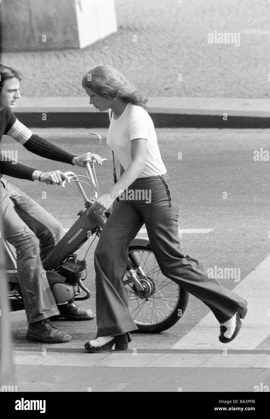 Negli anni settanta, foto in bianco e nero, persone giovane ragazza attraversa la strada, giovane uomo alla guida di un mofa, T-shirt, pantaloni, pullover, jeans pantaloni, di età compresa tra i 18 e i 22 anni Foto Stock