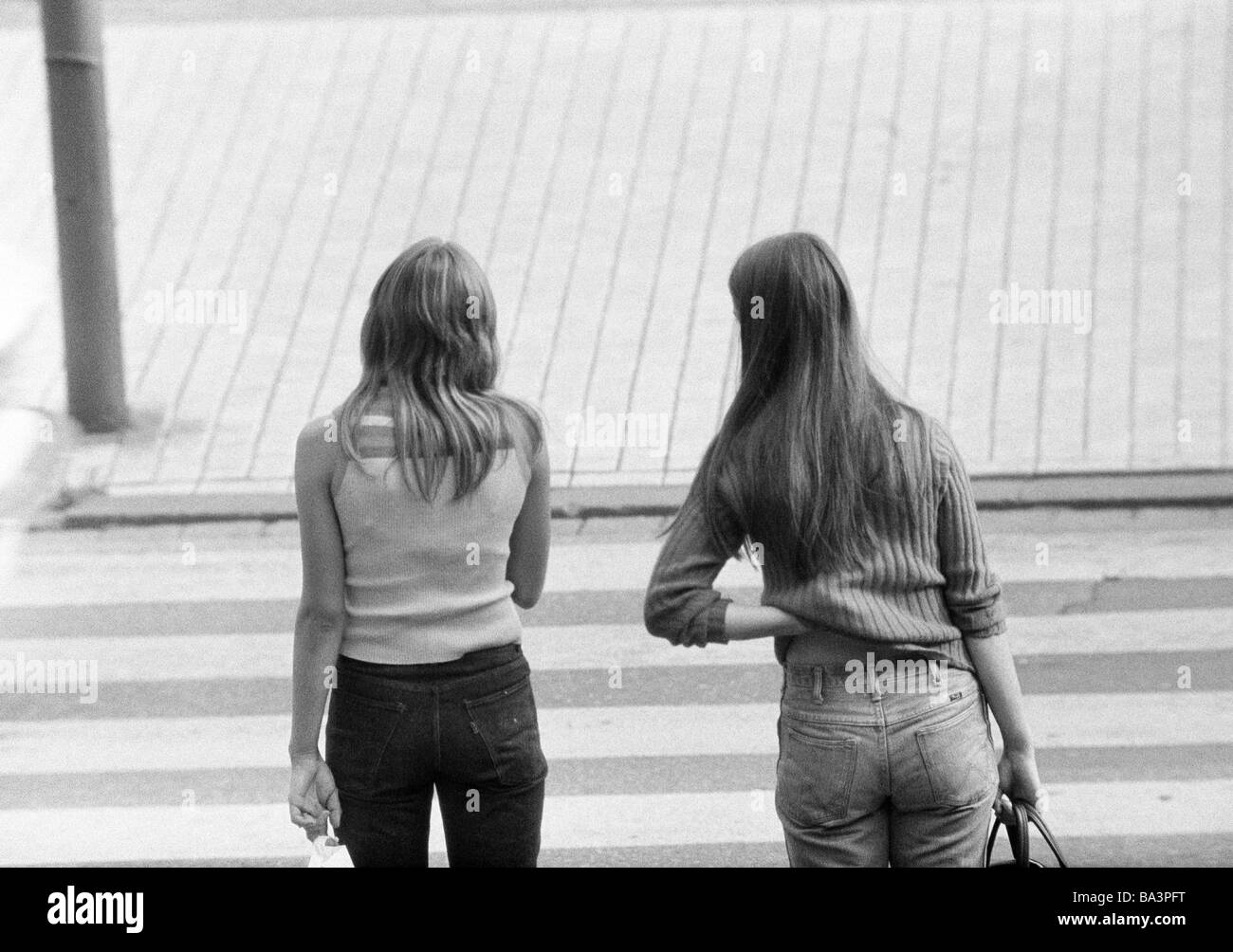 Negli anni settanta, foto in bianco e nero, persone, due giovani ragazze di strada, pullover, teeshirt, jeans pantaloni, in attesa di una zebra crossing, di età compresa tra i 18 e i 22 anni Foto Stock
