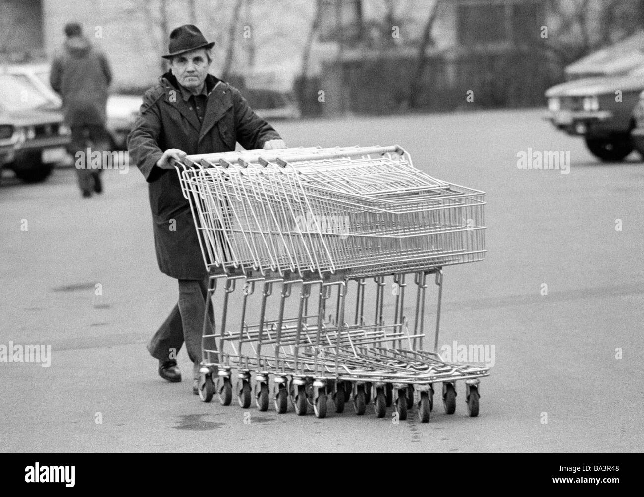 Ottanta, foto in bianco e nero, economia, commercio al dettaglio, shopping center, uomo anziano spinge diversi carrelli di shopping attraverso un parcheggio al punto di raccolta, di età compresa tra 65 a 70 anni Foto Stock