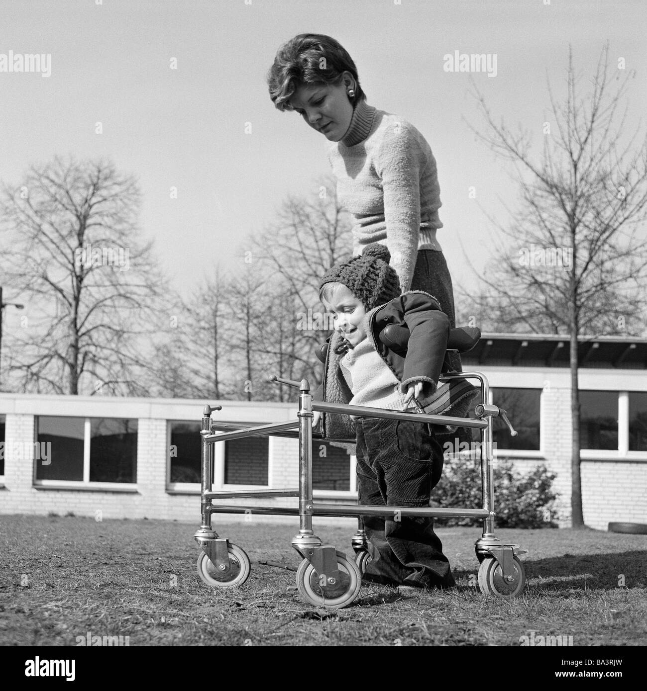 Negli anni settanta, foto in bianco e nero, persone di handicap fisici, fisioterapista assiste bambina in pochi esercizi in un camminatore su ruote, di età compresa tra i 20 e i 30 anni di età compresa tra 3 e 4 anni, Angelika, Ute, Scuola Speciale Alsbachtal, D-Oberhausen, D-Oberhausen-Sterkrade, la zona della Ruhr, Renania settentrionale-Vestfalia Foto Stock
