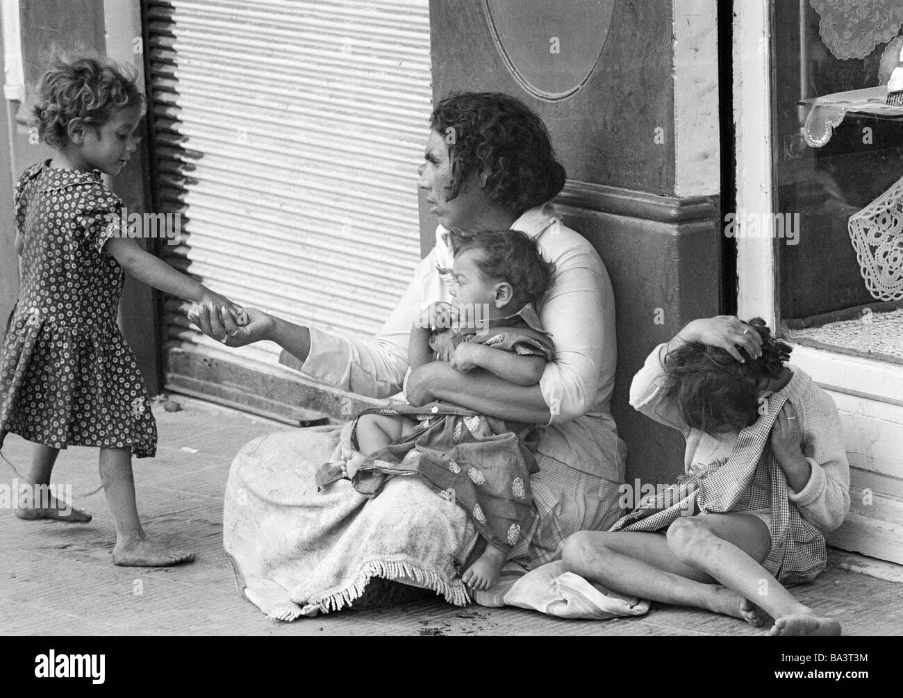 Negli anni settanta, foto in bianco e nero, persone poorness, mendicante-donna si siede sul bordo della strada con tre bambini, una ragazza presenta la sua un'inezia, di età compresa tra 35 a 45 anni di età compresa da 1 a 2 anni di età compresa tra i 4 e i 6 anni, Spagna, Valencia Foto Stock