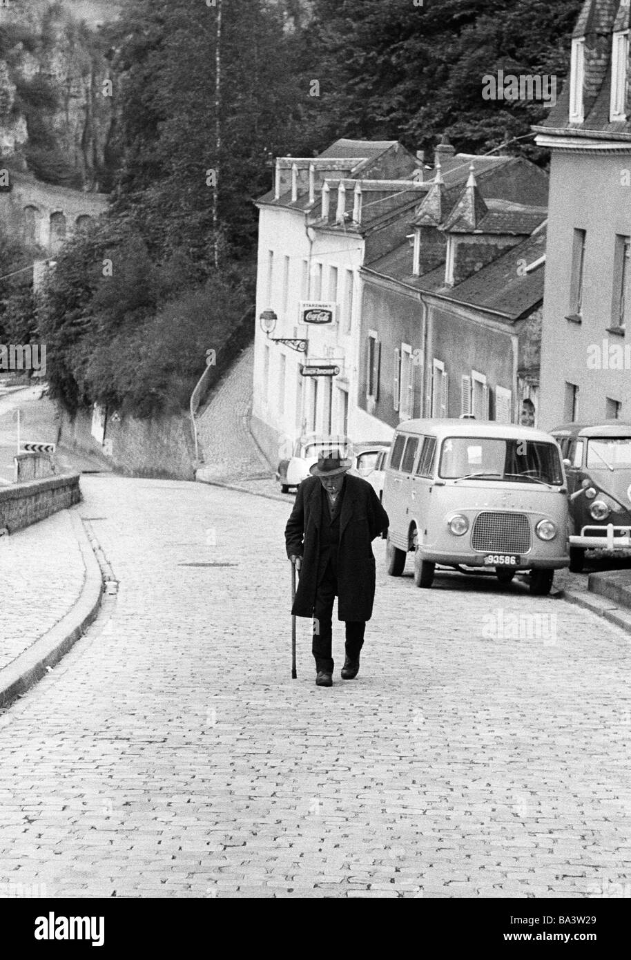 Anni sessanta, foto in bianco e nero, persone, senior, vecchio uomo cammina su una strada, un bastone da passeggio, cappotto, hat, gradiente, case, automobili, di età compresa tra 70 a 80 anni, Lussemburgo Foto Stock