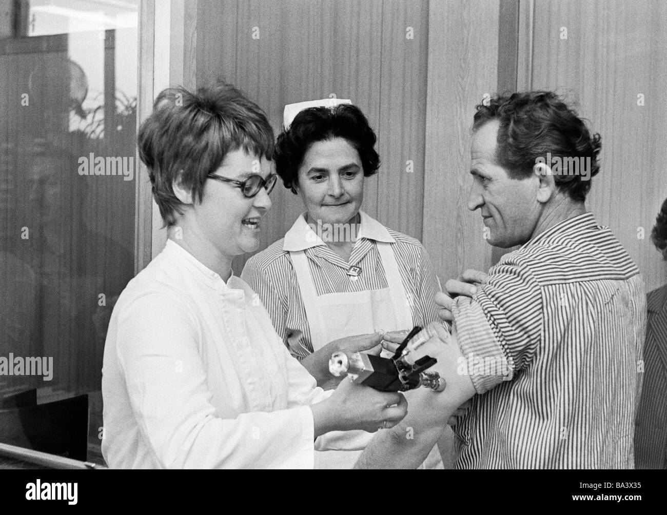 Negli anni settanta, foto in bianco e nero, persone, salute, precauzione, iniezione, virus influenzale vaccinazione, medico di sesso femminile di età compresa tra 30 a 40 anni, infermiera, di età compresa tra i 40-50 anni, paziente uomo, di età compresa tra i 45 e i 55 anni Foto Stock