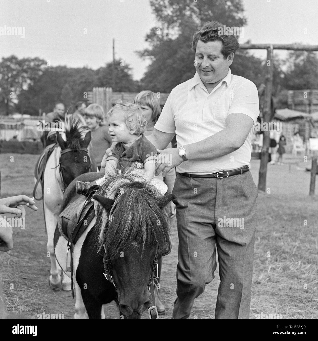Negli anni settanta, foto in bianco e nero, umana e animale, parco giochi per i bambini e percorsi per pony, uomo aiuta un ragazzino di bestride un cavallo, di età compresa tra i 30 e i 40 anni di età compresa tra i 2 e i 3 anni, Equus caballus ferus Foto Stock