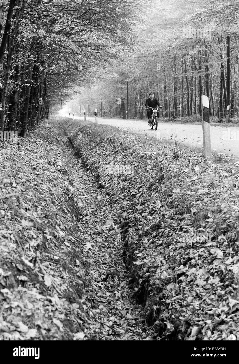 Negli anni settanta, foto in bianco e nero, Autunno, Foresta, country road, strada Fossato, uomo anziano pilota un ciclomotore, di età compresa tra 60 a 70 anni, D-Bottrop, D-Bottrop-Kirchhellen, Grafenwald, la zona della Ruhr, Renania settentrionale-Vestfalia Foto Stock
