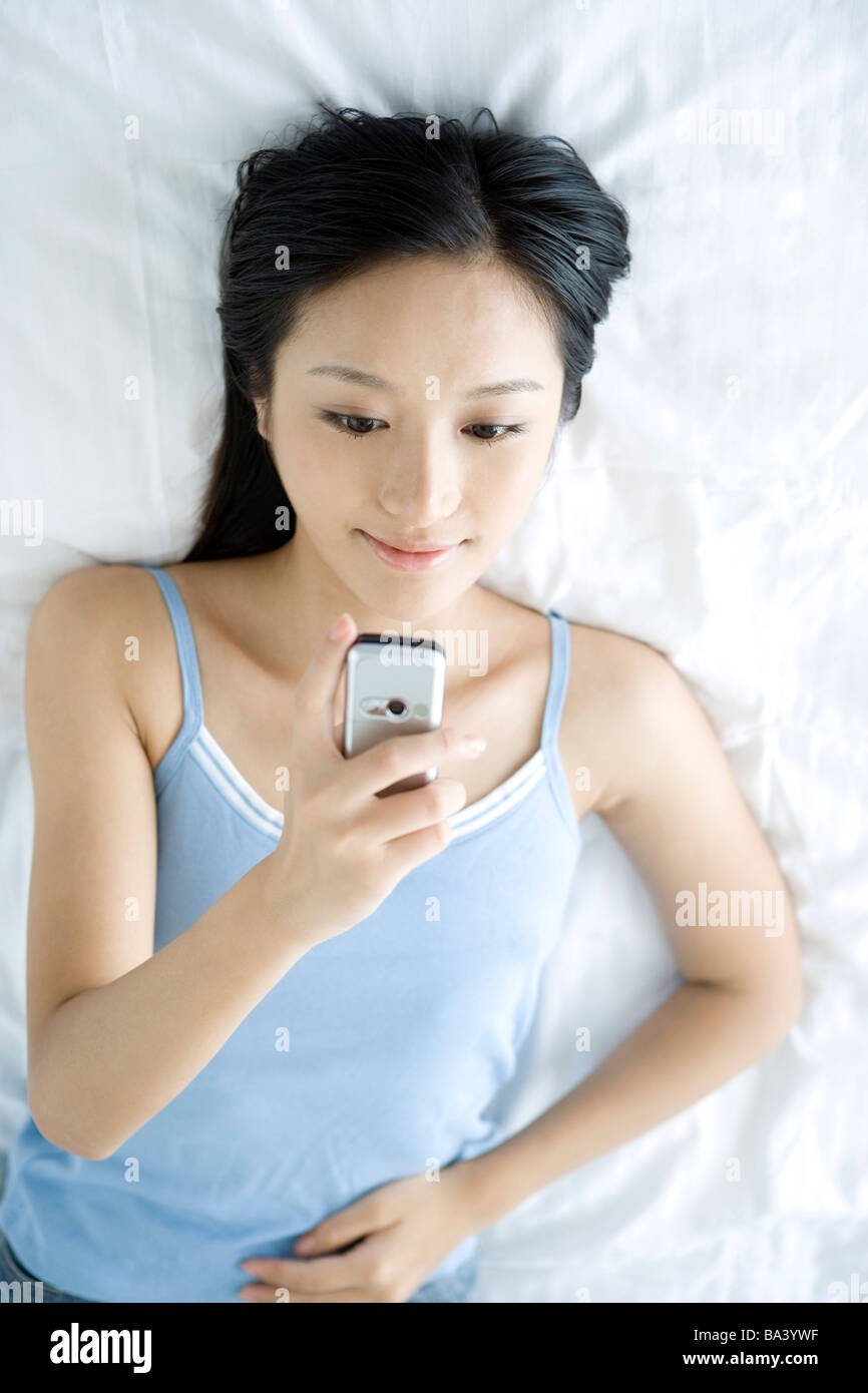 Giovane donna giaceva sul letto guardando al telefono cellulare Foto Stock