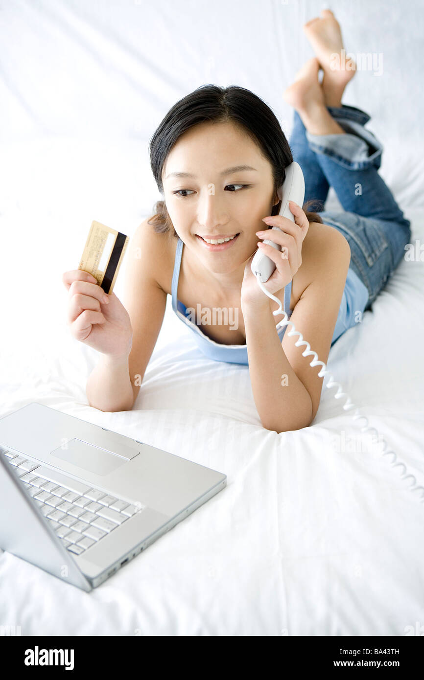 Giovane donna al telefono giacente sul letto azienda carta di credito Foto Stock