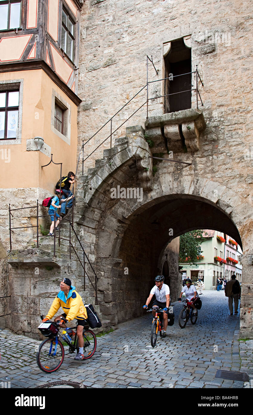Persone touring ciclismo Rothernburg entrando attraverso l'ingresso ad arco nel muro della città in Germania Foto Stock
